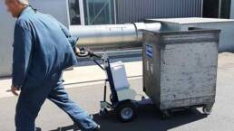 Hombre con remolcador M12 arrastrando un contenedor met&aacute;lico en el exterior de una f&aacute;brica